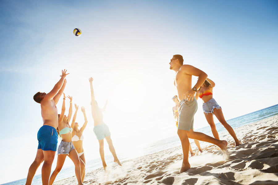 Group of friends playing game with ball at the beach on background of sunset sea